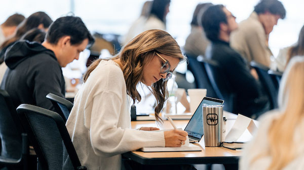 A Female student sitting at a desk and taking notes in a Watermark Institute teaching session.
